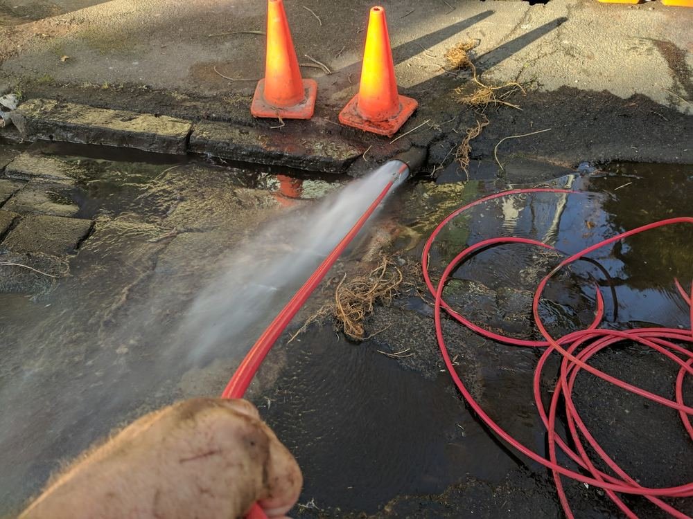 High-pressure water jetting cutting tree roots from a blocked stormwater drain