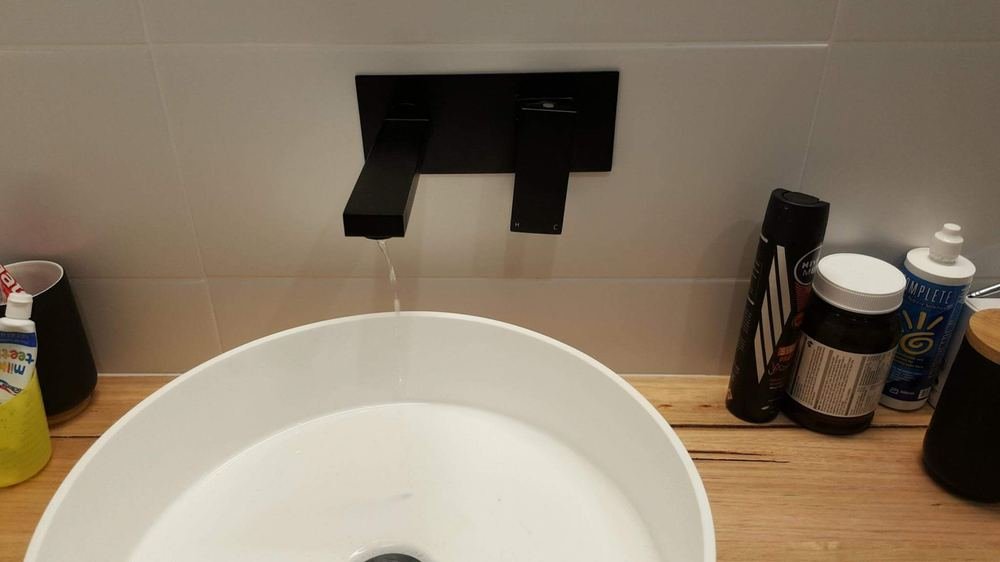 Matte black wall mixer running over a new round basin